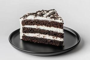 A slice of chocolate cake with white frosting and chocolate sprinkles on a black plate, isolated on a white background. photo