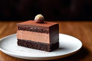 A single slice of decadent chocolate mousse cake with a chocolate sphere on top, dusted with cocoa powder and served on a white plate on a wooden table. photo