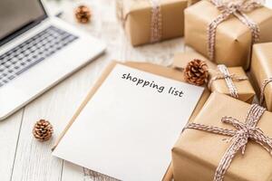 Preparing a holiday Christmas shopping list next to wrapped gifts and a laptop photo