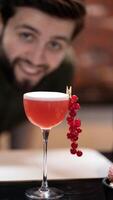 Smiling bartender looking at camera and presenting cocktail adorned with fresh red currants photo