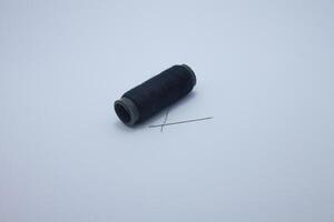 isolated spool of black thread and sewing needle photo