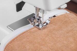 Modern sewing machine special presser foot with beige fabric and zipper, closeup photo