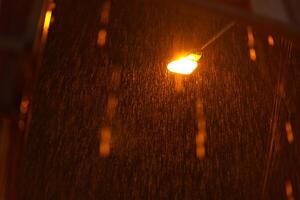 Glowing light bulb is hanging orange. Car parking indicator blinking at night on highway.It is raining heavily. The light of the lantern illuminates the drops of rainwater. photo