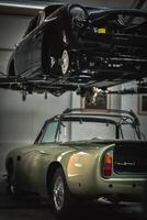 Classic, vintage, British car being restored on a ramp with visible rear axle and stripped car underneath photo
