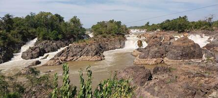 Scenic view of cascading waterfalls surrounded by rocky terrain and lush greenery under a partly cloudy sky. photo