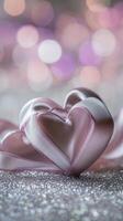 Two intertwined hearts created from delicate satin ribbon, placed on a silver glittering surface with soft pink and purple bokeh in the background photo