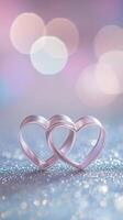 Two intertwined hearts created from delicate satin ribbon, placed on a silver glittering surface with soft pink and purple bokeh in the background photo