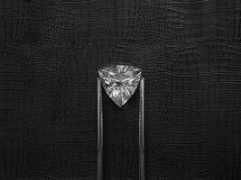 Cut Beautiful diamond held by tweezers, on a black leather background photo