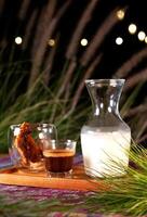 Caramel, Coffee and Milk served on a wooden tray at night with a blurry background showing bokeh lights and green grass. photo