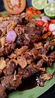 Delicious goat satay with soy sauce and fried shallots, served with fresh tomato sambal, lime slices, and tomato on a banana leaf. photo