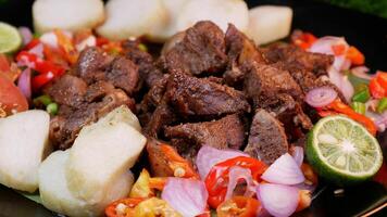 Grilled goat served complete with rice cakes, tomato slices, lime, and a sprinkle of fried shallots and red onions on a fresh banana leaf. photo