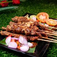 Juicy chicken satay with peanut sauce, garnished with fried shallots, and served with fresh tomato slices, shallots, chilies, and lime on a banana leaf. photo