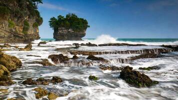 The beauty of Karang Bokor Beach, Sawarna, Banten. Large rock decorated with trees in the middle of the sea are the main attraction of this view with the crashing waves add to the dynamic impression. photo