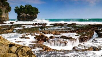 The beauty of Karang Bokor Beach, Sawarna, Banten. Large rock decorated with trees in the middle of the sea are the main attraction of this view with the crashing waves add to the dynamic impression. photo