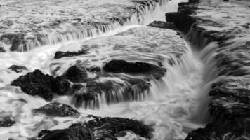 The crashing waves at Karang Bokor Sawarna Beach flowing over the coral rocks become a mini waterfall. The rough texture of the coral rocks and green moss add dimension to the scenery. photo