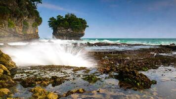 The beauty of Karang Bokor Beach, Sawarna, Banten. Large rock decorated with trees in the middle of the sea are the main attraction of this view with the crashing waves add to the dynamic impression. photo