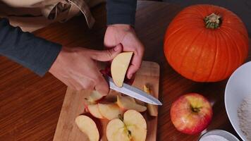 Hands peeling an apple with a knife on a wooden cutting board next to a pumpkin photo