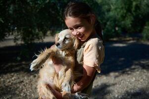 Girl joyfully holding her beloved dog under the sunlit trees in a serene outdoor setting, capturing the essence of friendship and happiness through a heartwarming display of affection and playfulness. photo