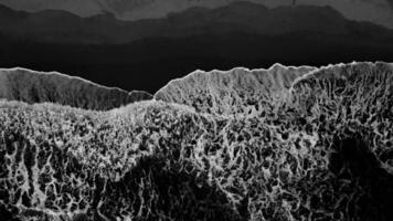 An artistic black and white aerial view shows large waves crashing against a sandy beach, creating interesting patterns on Sawarna Beach, Banten, Indonesia. photo
