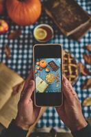 Capturing a cozy autumn scene with smartphone showing pumpkin pie on checkered tablecloth, surrounded by seasonal decor photo