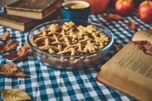 Cozy autumn scene with homemade apple pie accompanied by a hot drink and books, set on a checkered tablecloth for a warm, inviting setting perfect for a fall afternoon relaxation. photo