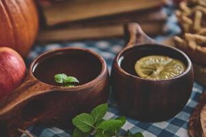 Rustic autumn drinks in wooden cups adorned with mint and lemon, set on a cozy gingham tablecloth with a backdrop of apples and pumpkin, creating an inviting harvest festival atmosphere. photo