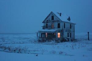 Old abandoned house standing on a snowy field at twilight photo