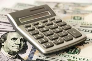 Calculator lying on one hundred dollar bills calculating savings photo