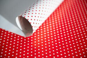 Red and white polka dot wrapping paper rolled on a surface, showcasing a classic and festive pattern ideal for gifts and crafts. Contrast between red background and white dots creates a vibrant look. photo