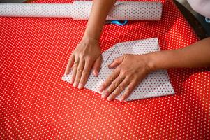 Hands folding polka dot paper on a red background in a pattern wrapping design setup photo