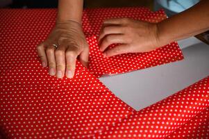 Close-up of hands carefully wrapping a present in vibrant red polka dot paper, capturing the essence of gift wrapping and festive preparation. photo
