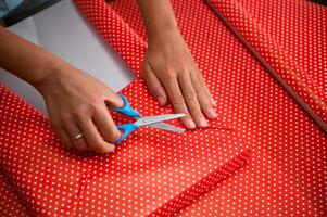 Hands using scissors to cut festive red and white polka dot wrapping paper, preparing for gift wrapping occasion such as Christmas or birthdays in a creative and organized manner. photo