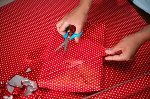 Hands wrapping a gift with red dotted paper using scissors for precise cuts during festive gift preparation at home photo