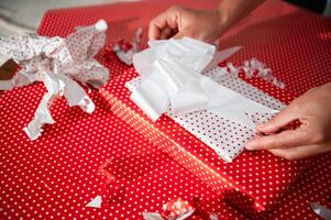 Hands wrapping a festive gift in vibrant red polka dot paper creating a joyful holiday atmosphere photo