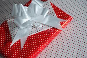 Festive gift box with a vibrant red polka dot pattern and elegant white ribbon resting on matching dot background photo