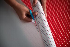 Hands cutting red and white polka dot wrapping paper during a DIY project. Focus on creativity, precision, and festive preparation, emphasizing the personal touch in gift wrapping. photo