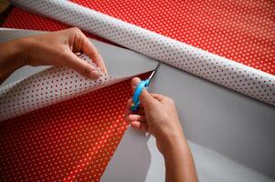 Person wrapping a gift with red and white polka dot wrapping paper using scissors photo
