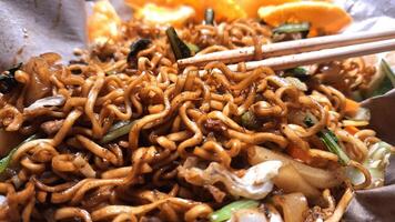 Savory Fried Noodles on Rice Paper with Meatballs, Sliced Chicken, Fresh Vegetables such as Mustard Greens, Cabbage, and Carrots, Served with Crispy Crackers, Ready to be Enjoyed using Chopsticks. photo