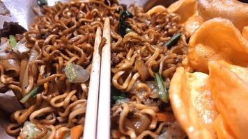 A Dish of Fried Noodles on Rice Paper Accompanied by Meatballs, Sliced Chicken, Pieces of Green Vegetables and Crispy Crackers, Creates a Delicious Taste Sensation and is Enjoyed using Chopsticks. photo