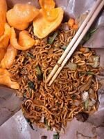A Dish of Fried Noodles on Rice Paper Accompanied by Meatballs, Sliced Chicken, Pieces of Green Vegetables and Crispy Crackers, Creates a Delicious Taste Sensation and is Enjoyed using Chopsticks. photo