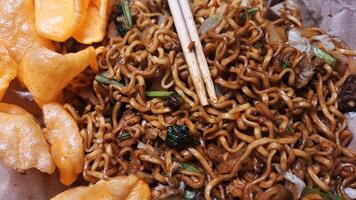Savory Fried Noodles on Rice Paper with Meatballs, Sliced Chicken, Fresh Vegetables such as Mustard Greens, Cabbage, and Carrots, Served with Crispy Crackers, Ready to be Enjoyed using Chopsticks. photo