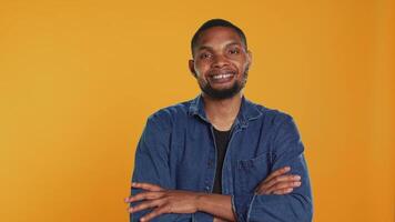 Portrait of african american casual man posing against orange background, showing confidence and determination in studio. Charismatic serious guy in stylish clothes. Camera A. video