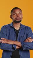 Vertical Portrait of african american casual man posing against orange background, showing confidence and determination in studio. Charismatic serious guy in stylish clothes. Camera B. video