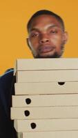 Vertical Clumsy deliveryman dropping a huge stack of pizza boxes in studio, wasting a lot of food and making a mess. Young distressed man makes a mistake and spills a large pile of fast food. Camera A. video