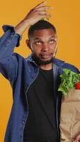 Vertical Playful vegan guy dancing with an apple placed on his head, having fun trying to be balanced and not drop it. Confident happy man recommending homegrown local fresh produce. Camera B. video