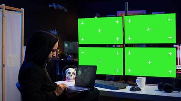Man writing code on laptop in front of isolated screen PC monitors, trying to get past security systems. Hacker using chroma key computer and notebook to make scripts that can hack devices, camera B video
