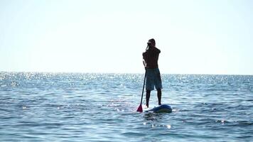 Man Sup Sea. Strong athletic man learns to paddle sup standing on board in open sea ocean on sunny day. Summer holiday vacation and travel concept. Aerial view. Slow motion video