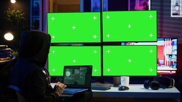 Man writing code on laptop in front of isolated screen PC monitors, trying to get past security systems. Hacker using chroma key computer and notebook to make scripts that can hack devices, camera A video