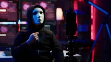 Focus on camera on phone on tripod used by hacker concealing identity filming ransom in hidden base. Close up of smartphone used by cybercriminal with mask to record blackmail footage, camera A video