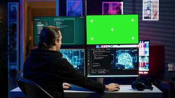 Hacker using green screen monitor and artificial intelligence to write spyware software gathering data from users. Scammer in apartment using AI and mockup PC display to do fraud using AI, camera A video